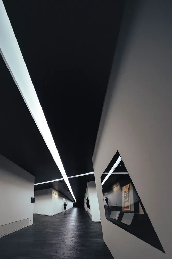 Interior angular e dramático de um edifício de Libeskind, com raios de luz atravessando fendas, criando padrões complexos no chão.