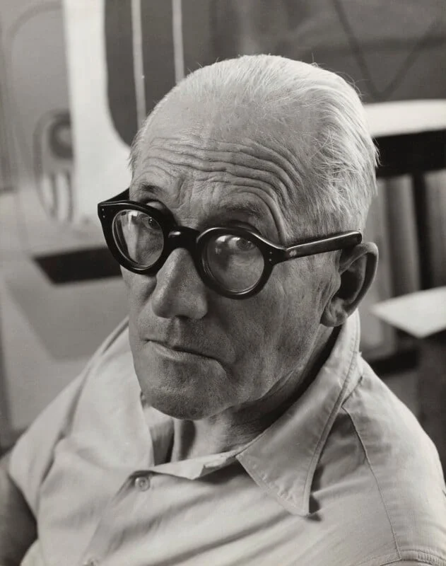 Retrato icônico de Le Corbusier, com seus óculos redondos característicos.