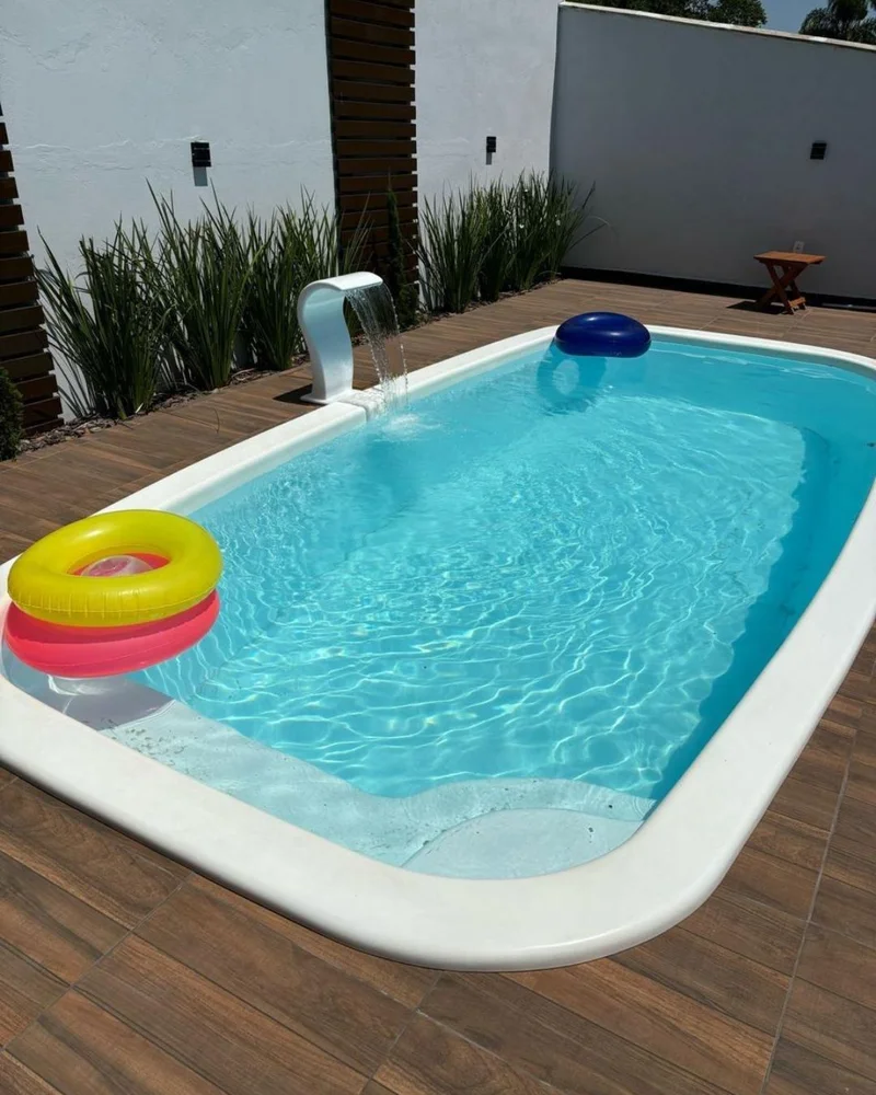 Piscina de fibra retangular com prainha, instalada em um deck de madeira com espreguiçadeiras e um belo jardim ao redor.