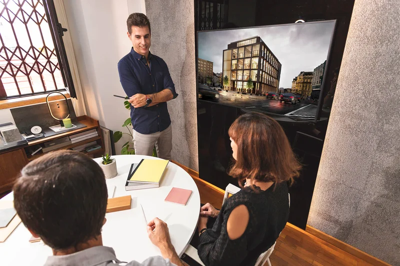 Arquiteto em uma reunião com clientes, discutindo o programa de necessidades com plantas e anotações sobre a mesa.