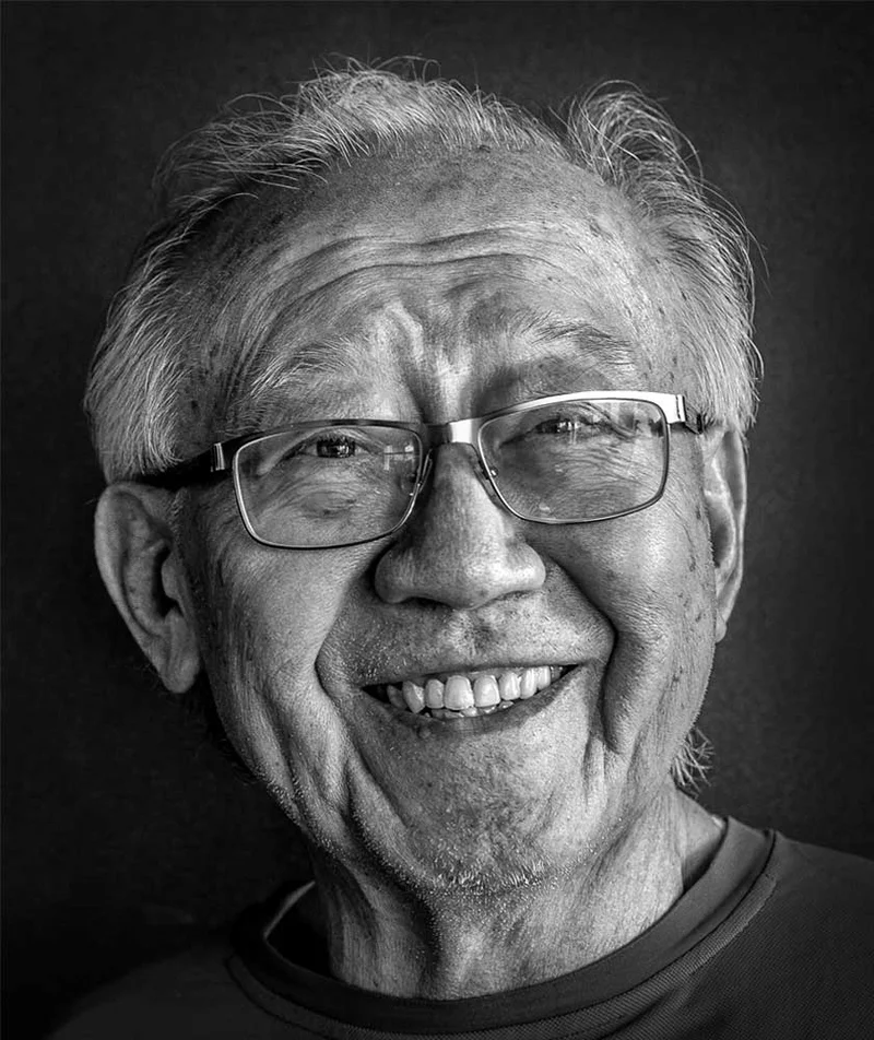 Ruy Ohtake sorrindo, com um de seus edifícios coloridos ao fundo.